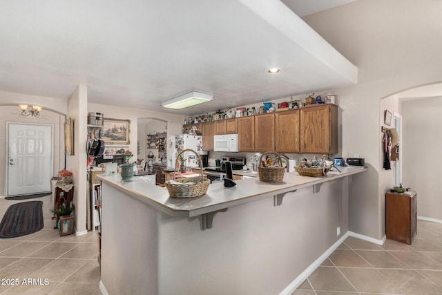 kitchen with white appliances, a breakfast bar area, brown cabinetry, light countertops, and light tile patterned floors