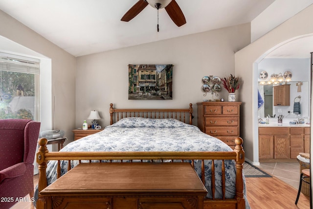 bedroom featuring a ceiling fan, connected bathroom, arched walkways, light wood-style floors, and lofted ceiling