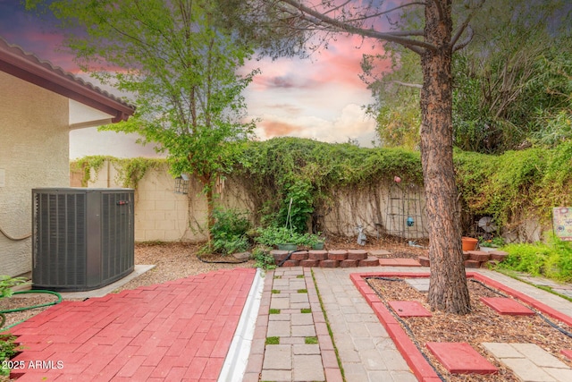 patio terrace at dusk featuring central AC unit and a fenced backyard