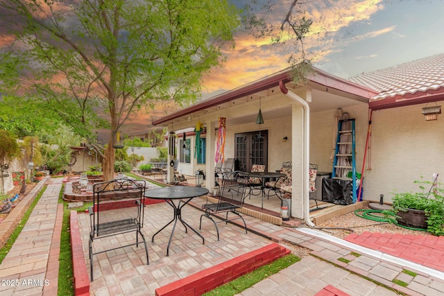 patio terrace at dusk with french doors, outdoor dining area, and fence