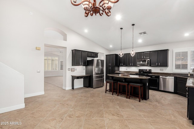 kitchen featuring pendant lighting, stainless steel appliances, a kitchen island, dark cabinetry, and a kitchen bar