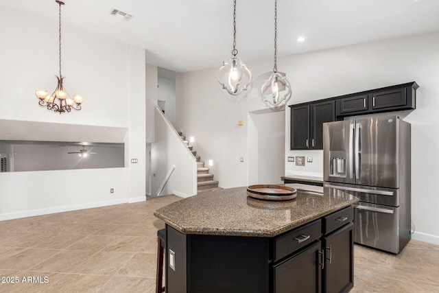 kitchen with dark stone counters, stainless steel fridge with ice dispenser, a center island, decorative light fixtures, and dark cabinetry