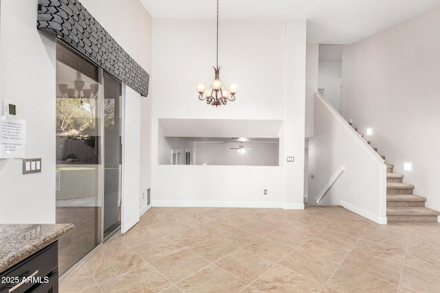 unfurnished dining area featuring ceiling fan with notable chandelier, a towering ceiling, baseboards, and stairs