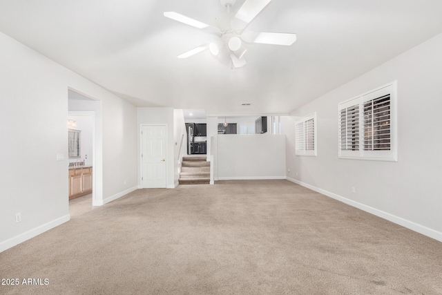 empty room with baseboards, stairway, ceiling fan, and light colored carpet