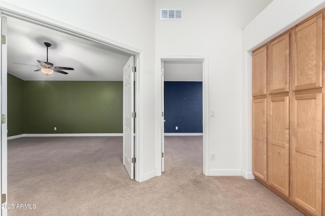 hallway with baseboards, visible vents, and light colored carpet