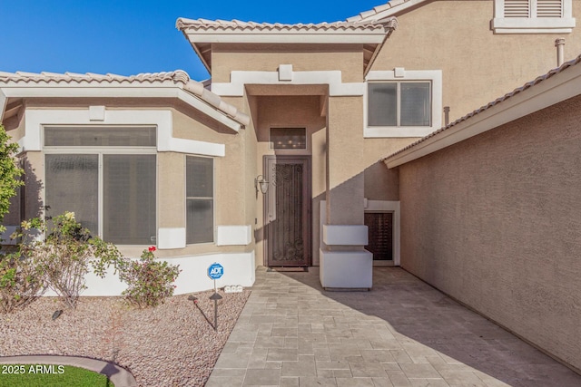 entrance to property with a patio, a tiled roof, and stucco siding