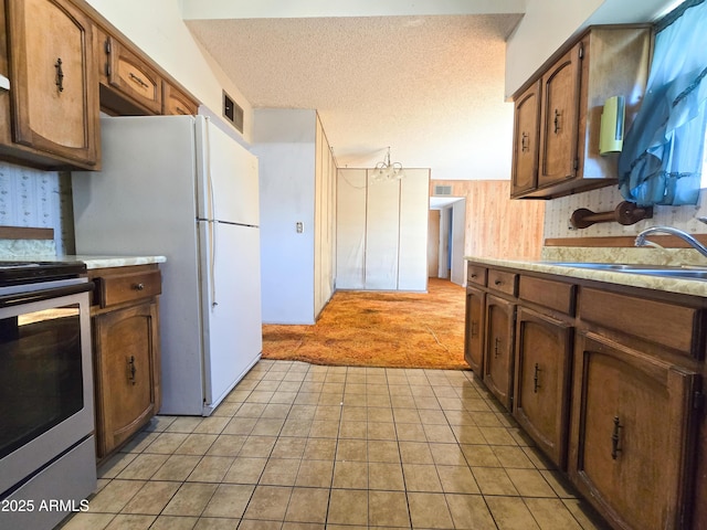 kitchen with wooden walls, light carpet, stainless steel range with electric stovetop, sink, and white refrigerator