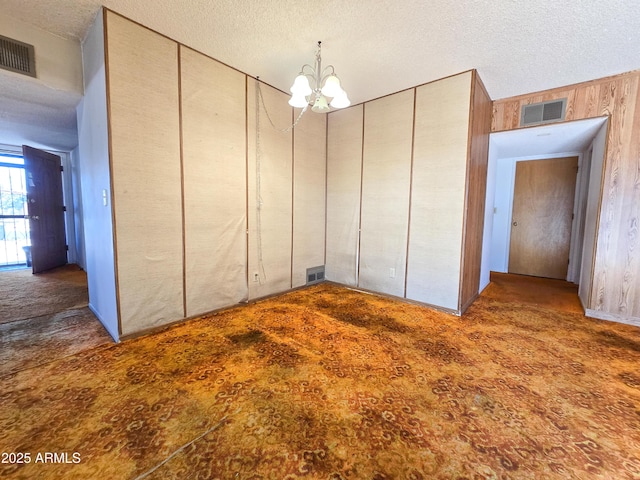 unfurnished bedroom featuring a chandelier, dark carpet, wooden walls, and a textured ceiling