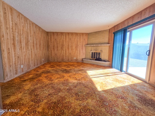 unfurnished living room featuring a brick fireplace, a textured ceiling, and wood walls