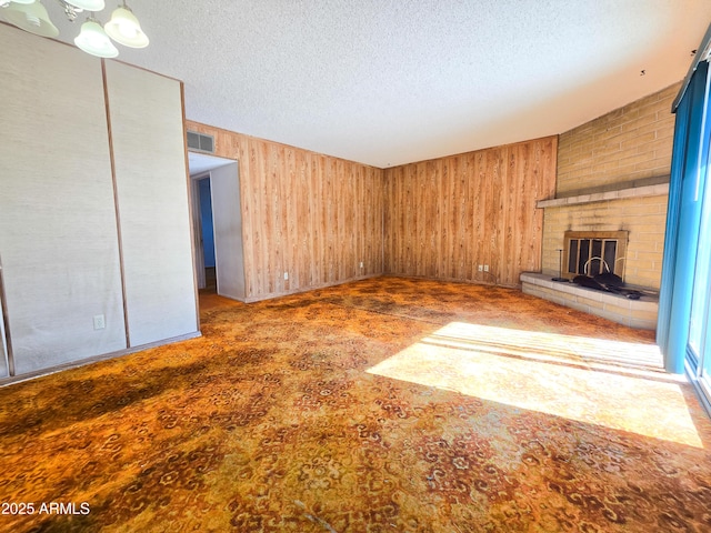 unfurnished living room featuring a brick fireplace, a textured ceiling, carpet, and wooden walls