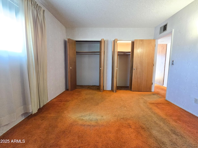 unfurnished bedroom with light carpet, a textured ceiling, and two closets