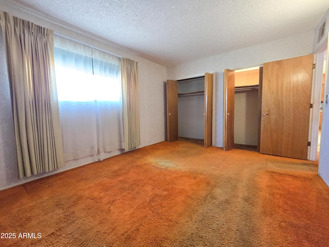 unfurnished bedroom with multiple closets, light colored carpet, and a textured ceiling