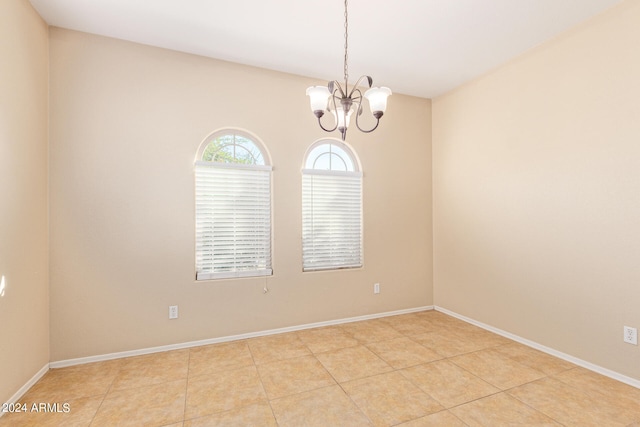 tiled spare room featuring a chandelier