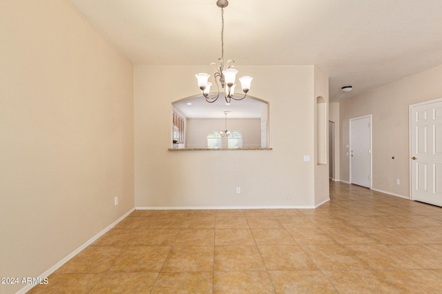 tiled spare room featuring an inviting chandelier