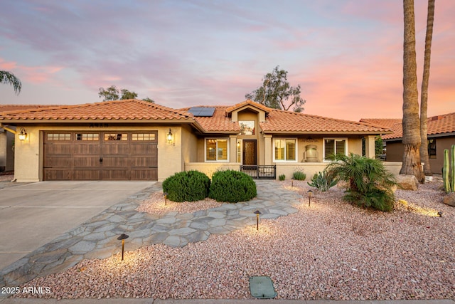 mediterranean / spanish house with solar panels, stucco siding, an attached garage, driveway, and a tiled roof