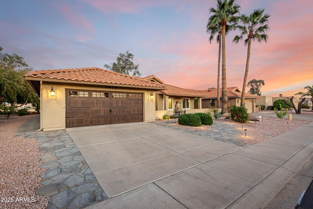 mediterranean / spanish house with a garage, concrete driveway, a tile roof, and stucco siding