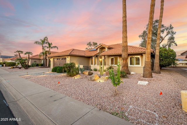 mediterranean / spanish house with concrete driveway, a tile roof, an attached garage, roof mounted solar panels, and stucco siding