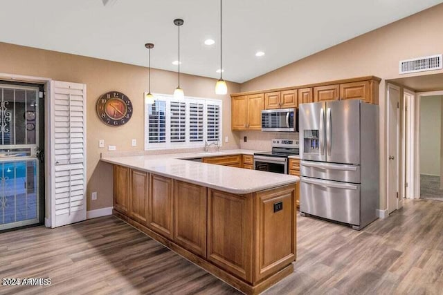 kitchen with hardwood / wood-style floors, stainless steel appliances, backsplash, hanging light fixtures, and kitchen peninsula