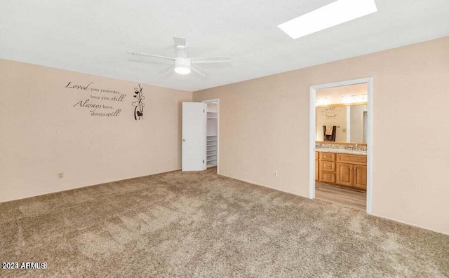 unfurnished bedroom with ensuite bathroom, light colored carpet, ceiling fan, and a skylight