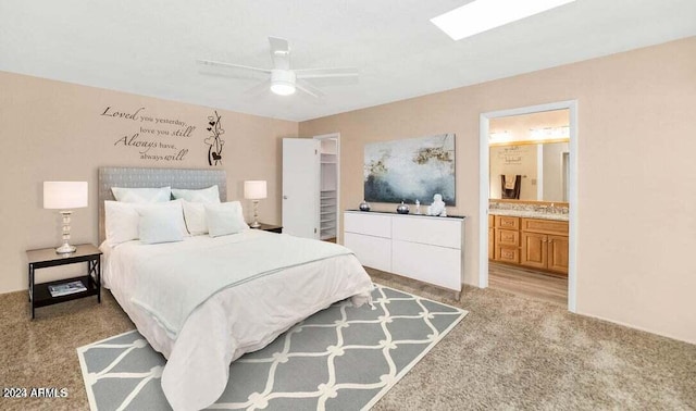 carpeted bedroom featuring ceiling fan, ensuite bathroom, and a skylight