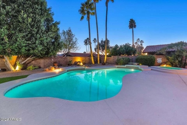 pool at dusk with an in ground hot tub and a patio