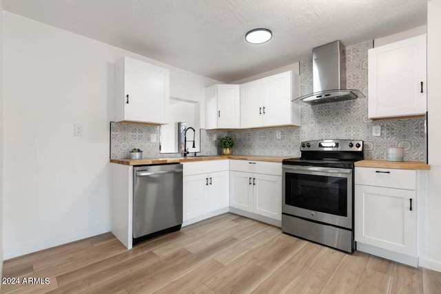 kitchen featuring butcher block counters, wall chimney range hood, white cabinetry, and stainless steel appliances