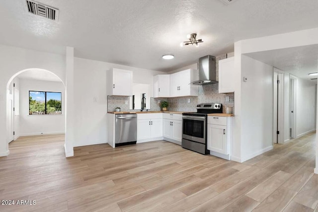 kitchen featuring wall chimney exhaust hood, white cabinetry, light hardwood / wood-style flooring, appliances with stainless steel finishes, and a textured ceiling