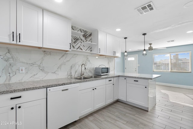 kitchen featuring white dishwasher, sink, kitchen peninsula, white cabinetry, and decorative backsplash