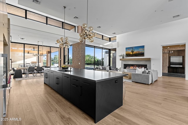7341 E Sunnyside Dr, Scottsdale, AZ 85260 - kitchen with dark cabinetry, a warm lit fireplace, a sink, light wood finished floors, and a high ceiling
