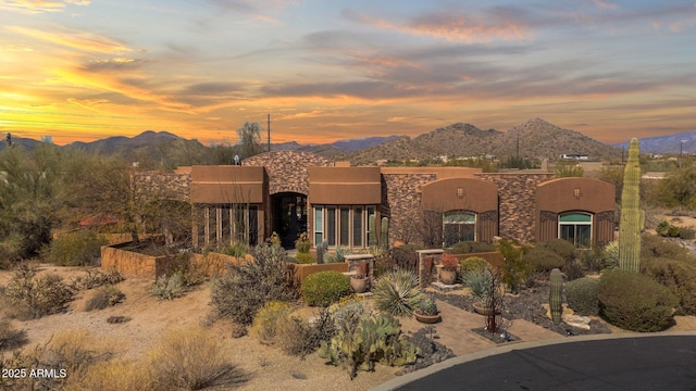 pueblo revival-style home with stone siding, a mountain view, and stucco siding