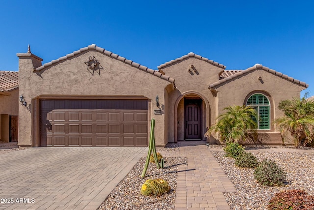 mediterranean / spanish-style home with a garage, a tiled roof, decorative driveway, and stucco siding