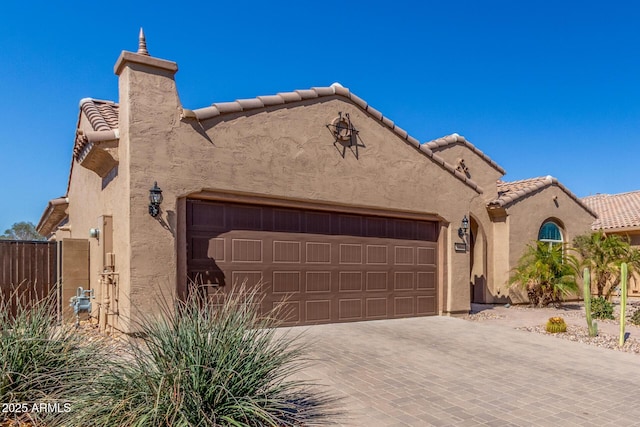 mediterranean / spanish-style house with a garage, a tiled roof, decorative driveway, and stucco siding