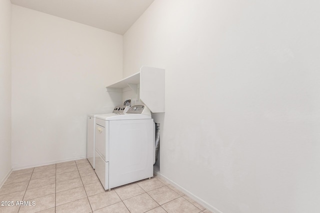 clothes washing area featuring washing machine and dryer, laundry area, light tile patterned flooring, and baseboards