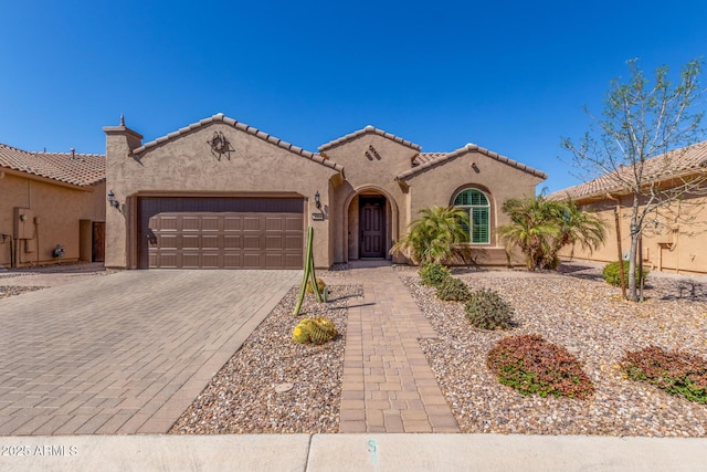 mediterranean / spanish-style home with a garage, decorative driveway, a tiled roof, and stucco siding