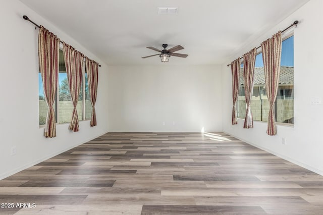 empty room featuring a ceiling fan, a healthy amount of sunlight, visible vents, and wood finished floors