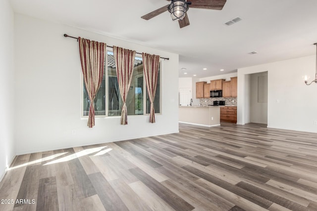 unfurnished living room featuring ceiling fan with notable chandelier, light wood finished floors, visible vents, and recessed lighting