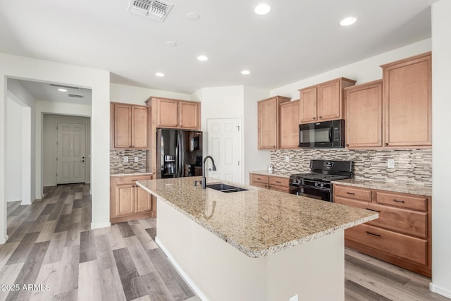 kitchen with a sink, visible vents, black appliances, light wood finished floors, and an island with sink