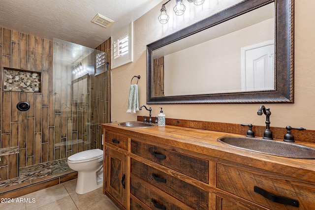 bathroom featuring toilet, tile patterned floors, a textured ceiling, a tile shower, and vanity