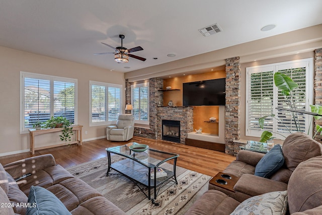 living room featuring a stone fireplace, hardwood / wood-style floors, and ceiling fan