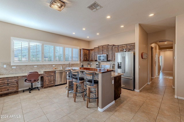 kitchen featuring light stone countertops, appliances with stainless steel finishes, decorative backsplash, and a center island