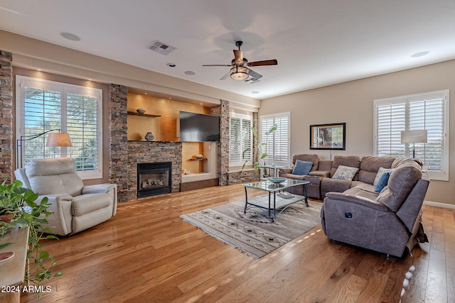 living room featuring a stone fireplace, hardwood / wood-style flooring, and ceiling fan