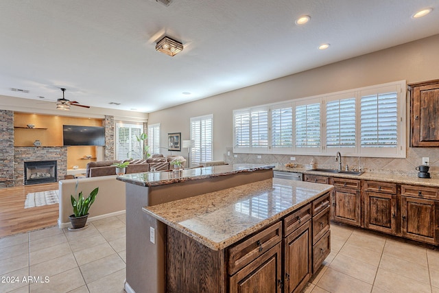 kitchen with sink, light stone countertops, ceiling fan, a stone fireplace, and a kitchen island