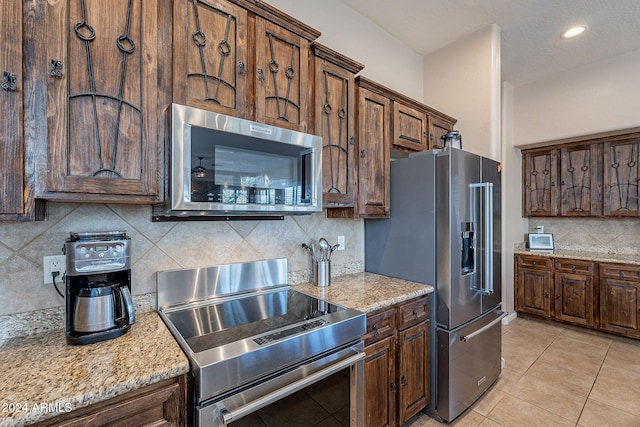 kitchen featuring light tile patterned flooring, backsplash, appliances with stainless steel finishes, and light stone countertops