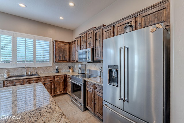 kitchen with light tile patterned floors, sink, tasteful backsplash, light stone countertops, and appliances with stainless steel finishes