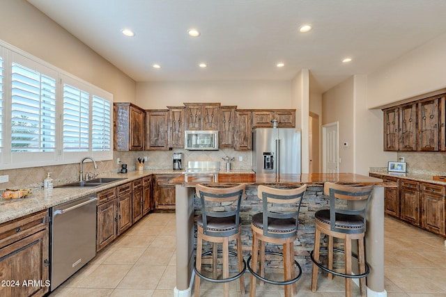 kitchen featuring a kitchen bar, stainless steel appliances, light stone counters, a center island, and sink