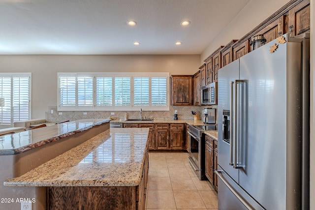 kitchen featuring light stone counters, sink, a kitchen island, and appliances with stainless steel finishes