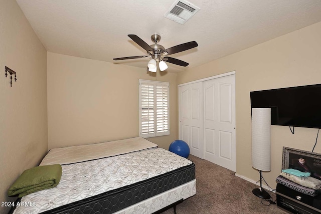 bedroom featuring a textured ceiling, dark carpet, ceiling fan, and a closet