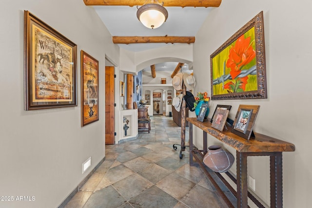 hall featuring arched walkways, beam ceiling, stone tile floors, and baseboards