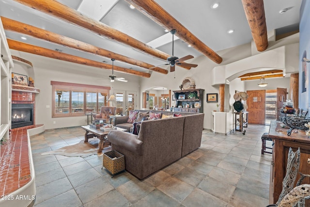 living room with ceiling fan, beamed ceiling, recessed lighting, arched walkways, and a glass covered fireplace