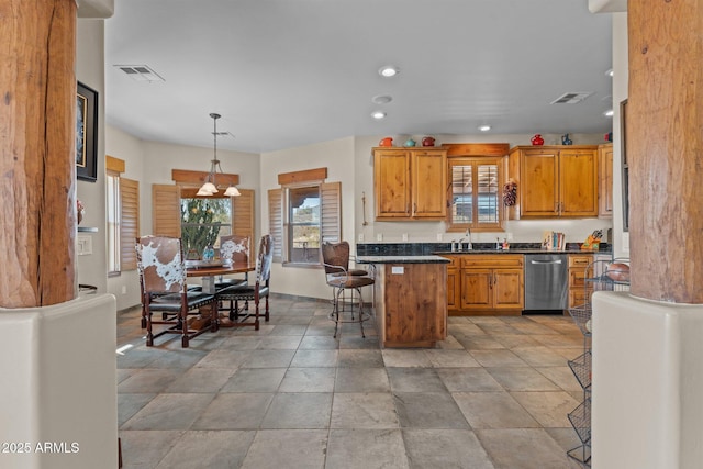 kitchen featuring a kitchen bar, a sink, stainless steel dishwasher, dark countertops, and brown cabinetry